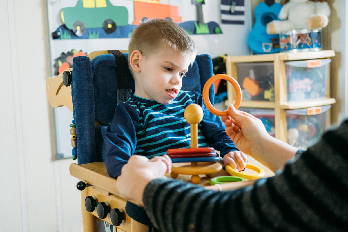 Activities for kids with disabilities. Preschool Activities for Children with Special Needs. Boy with with Cerebral Palsy in special chair play with mom at home.